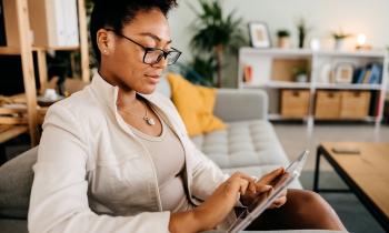 Une femme assise sur son canapé consulte un dossier sur sa tablette