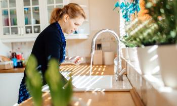 Une femme debout dans sa cuisine fait couler de l'eau dans son évier 
