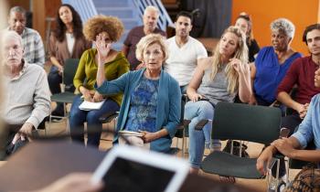Une femme assise dans l'assemblée lève la main pour parler lors d'une assemblée générale de copropriété