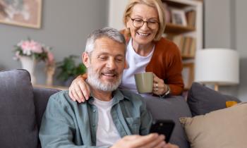 Un couple de retraités regarde des informations sur un téléphone portable dans son salon