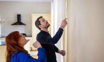 Un couple mesure la hauteur d'un mur de son logement à l'aide d'un mètre