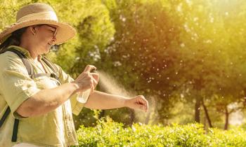 Une dame portant un chapeau vaporise un spray anti-moustiques sur son avant-bras, en extérieur