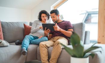 Un couple, dont la femme est enceinte, effectue des recherches sur tablette, installé sur son canapé