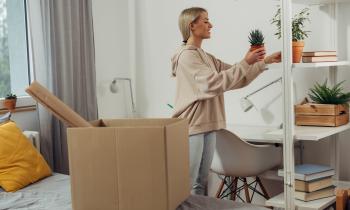 Une étudiante défait ses cartons et pose une plante sur une étagère pour la décorer