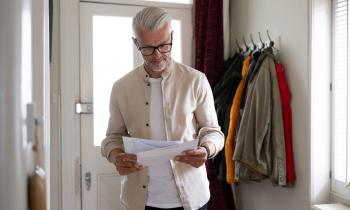 Un homme aux cheveux blancs lit un courrier qu'il vient de recevoir à son domicile