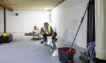 Un homme accroupi recherche les causes d'une inondation dans un sous-sol
