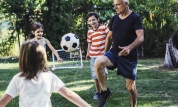 Des enfants jouent au foot dans leur jardin avec un homme d'âge mûr