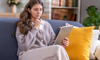 Une jeune femme étudie des documents sur une tablette, assise sur son canapé