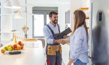 Une femme reçoit un ouvrier dans sa belle cuisine claire et lui serre la main. 