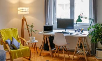 Chambre d'étudiant avec bureau, ordinateurs, fauteuil jaune et lampadaire allumé. 
