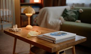 Petit appartement avec focus sur la table basse en bois brut, quelques livres et une lampe moderne jaune. 