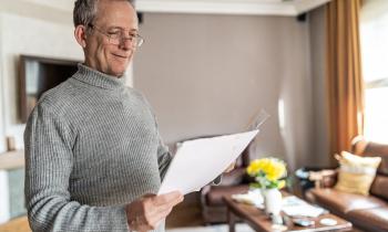 Un homme d'âge mûr examine un document debout dans son salon, avec le sourire