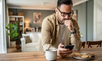 Un homme assis à la table de la cuisine apparait contrarié en lisant un message sur son téléphone