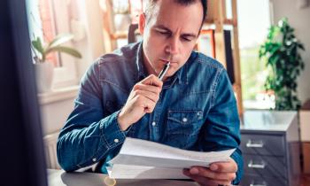 Un homme assis à son bureau vérifie avec attention le contenu du courrier qu'il tient dans la main