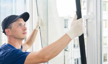 Un jeune professionnel en tenue de travail installe du double-vitrage sur la fenêtre d'un appartement