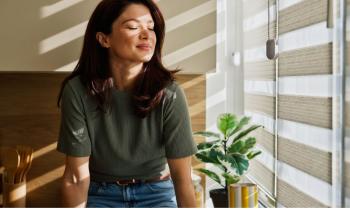 Femme profitant du soleil du matin à la maison près des stores de fenêtre 