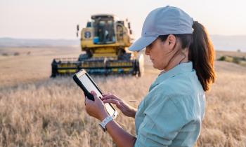 Une agricultrice tient une tablette numérique dans un champ agricole pour piloter son activité