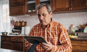 Un homme âgé se tient debout dans sa cuisine un peu ancienne, un cadre dans les mains