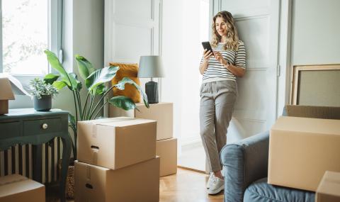 femme sur son téléphone dans un appartement entourée de cartons