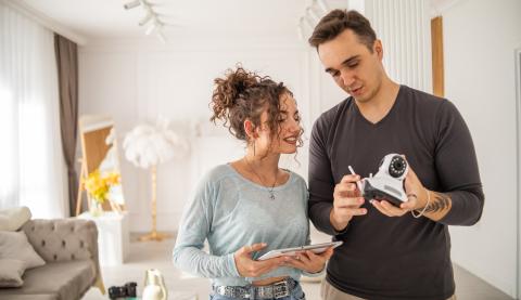 une jeune femme avec un jeune homme qui tient une camera de surveillance pour l'installer dans une maison