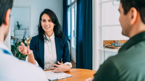 une femme devant un bureau fait face à deux hommes pour signer un docuement