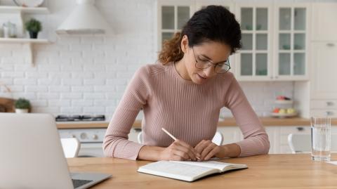 Jeune femme devant son ordi en train de prendre des notes