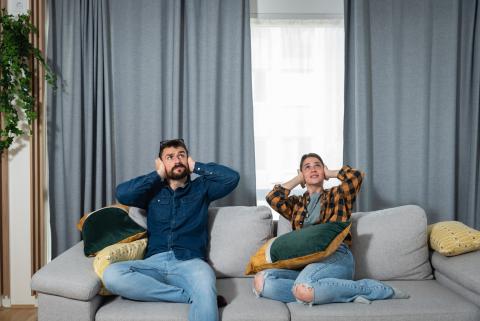 Jeune couple dans leur canapé, agacé par les nuisances sonores de leur appartement.