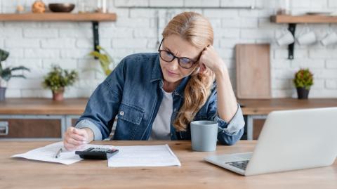 Femme blonde concentrée effectuant des calculs devant son pc, la tête en appui sur son bras