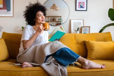 Célibataire assise sur son canapé avec à la main un livre et dans l'autre une tasse de thé