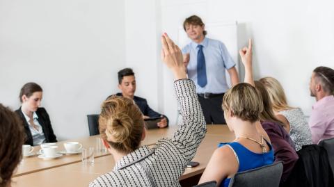 Des personnes sont réunies autour d'une table et lèvent la main pour voter, dans le cadre d'une réunion d'assemblée générale