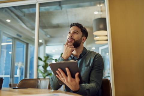 Un homme, réfléchissant, une tablette à la main