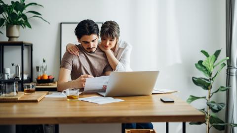 Un couple étudie un document devant un ordinateur, à son domicile. 