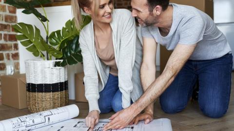 Un couple agenouillé sur le sol échange devant le plan de sa future maison