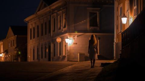 Une femme élégante marche seule sur le trottoir dans une rue sombre