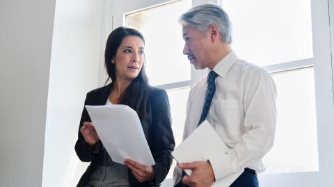 Un homme et une femme adossés contre une fenêtre échangent à propos d'un document