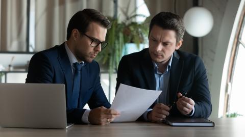 Un notaire donne des explications à son client au sujet du document qu'il tient dans la main, autour d'un bureau