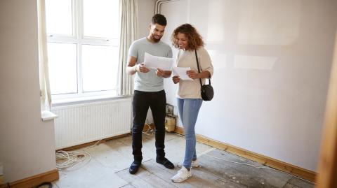 Un couple étudie des documents dans une pièce de son logement nécessitant des travaux de rénovation