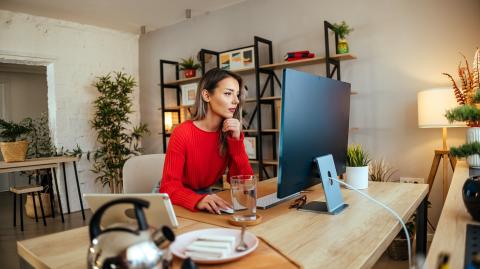 Une femme, installée à un bureau, consulte des documents sur son ordinateur personnel, dans son salon