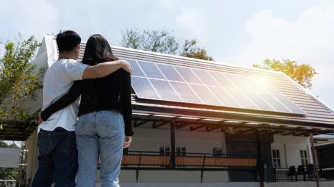 Couple enlacé, debout près de sa maison sur laquelle ont été installés des panneaux photovoltaïques