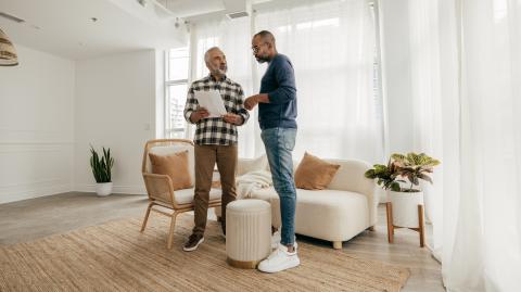 Deux hommes, debout dans un appartement, échangent au sujet d'un contrat