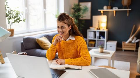 Une femme souriante télétravaille sur une table, dans son salon 