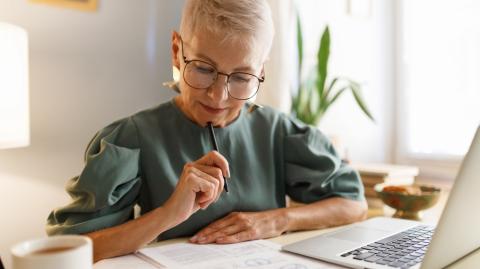 Une femme tente de comprendre un document au format papier, assise devant son ordinateur portable