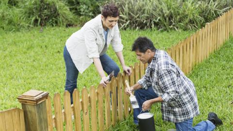 Un homme et une femme installent une petite clôture en bois commune en limite de leur terrain
