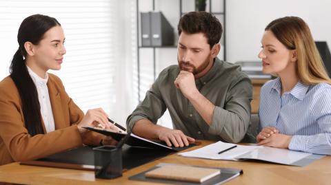 Un couple étudie avec attention un document au format papier présenté par son notaire au cours d'un rendez-vous