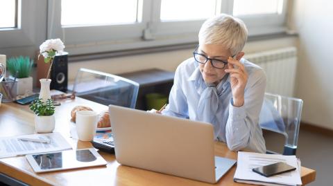 Une femme aux cheveux blancs très courts se charge de dossiers administratifs sur son pc portable