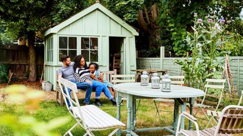 Une famille profite de son espace jardin, installée sur un banc devant un bel abri de jardin