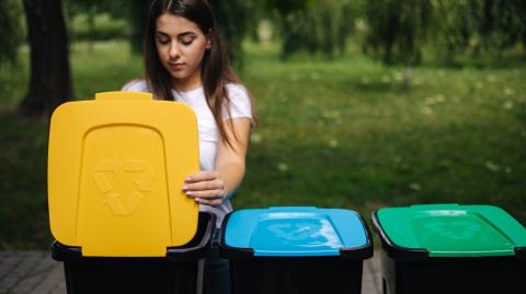 Une jeune femme aux cheveux longs jette un emballage dans le bac de tri jaune