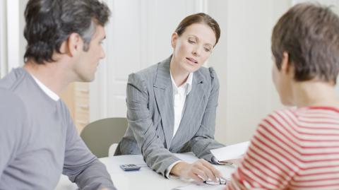 Une femme donne des explications à un couple de clients sur des documents au format papier
