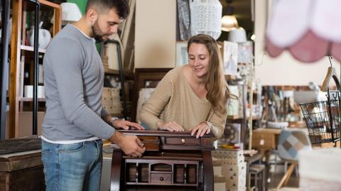Un jeune couple admire un petit secrétaire ancien en bois dans un magasin d'antiquités