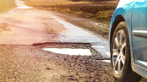 Une voiture emprunte une route endommagée, présentant plusieurs nids-de-poule remplis d'eau